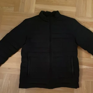 Svart pufferjacka från Jack & Jones - Säljer en svart pufferjacka från Jack & Jones i storlek M. Jackan har en stilren design med dragkedja och två praktiska fickor. Perfekt för höst och vinter, håller dig varm och bekväm. Passar både till vardags och lite finare tillfällen. 🖤ny priss 700
