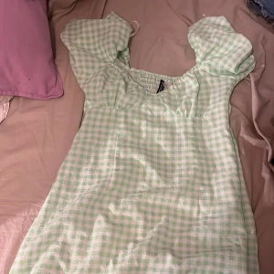 Grön rutig klänning från H&M Divided - Säljer en superfin grön rutig klänning från H&M Divided. Den har puffiga kortärmar och en söt, somrig stil. Perfekt för vår och sommar! Klänningen är i mycket bra skick och passar perfekt för en avslappnad dag ute eller en picknick i parken.