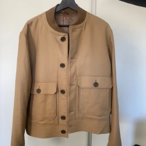 Beige jacka från Tiger of Sweden - Säljer en snygg beige jacka från Tiger of Sweden. Den har en stilren design med knappar framtill och två stora fickor med lock. Perfekt för höst och vår. Jackan är i mycket bra skick och passar både till vardags och lite finare tillfällen.