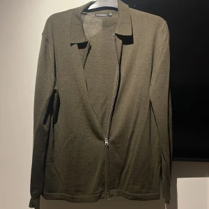 Olivgrön tröja med dragkedja från J.Lindeberg - Säljer en stilren olivgrön tröja från J.Lindeberg. Den har en praktisk dragkedja framtill och är tillverkad i ett mjukt material som känns skönt mot huden. Perfekt för både vardag och lite finare tillfällen. Passar bra till höst och vår! Nypris 2400 