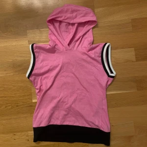 Rosa ärmlös huvtröja - Säljer en cool rosa ärmlös huvtröja i 100% bomull. Perfekt för sommardagar eller som ett lager på gymmet. Den har svarta och vita detaljer vid ärmhålen och en svart kant nedtill. 🤍