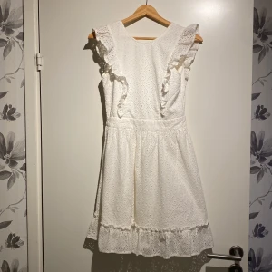 Vit klänning från Scotch & Soda - Säljer en superfin vit klänning från Scotch & Soda. Den har volanger på axlarna och en söt knytning i ryggen. Perfekt för sommarens fester eller midsommarfirandet! Klänningen är i ett vackert spetsmaterial och har en volangdetalj längst ner.