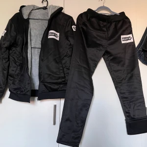 Svart träningsset  - Säljer ett svart träningsset helt nya Jackan har dragkedja och en grå fleecefodrad insida för extra värme. Byxorna är matchande och bekväma, perfekta för träning eller chill. Setet har en normal passform och är idealiskt för vintern 