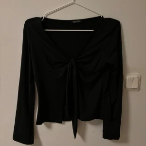 Svart långärmad topp från Missäy - Snygg svart långärmad topp från Missy med knytning framtill och öppen i magen. Perfekt för både vardag och fest. . Materialet känns mjukt och bekvämt mot huden. 