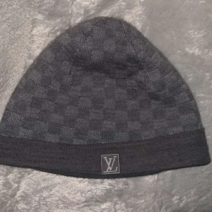 Grå mössa från Louis Vuitton - Säljer en snygg grå mössa från Louis Vuitton med ett diskret rutmönster. Den är i materialet ull och kashmir, gammal design på mössan som inte går att köpa den längre. Hör av er vid frågor!😇