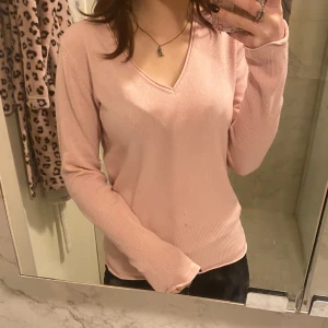 Rosa v-ringad långärmad - Säljer en superfin rosa tröja med v-ringning. Den är i bra skick men har ett litet hål på ryggen, typ 1mm så det märks knappt. Tröjan har långa ärmar och är gjord i ett mjukt material som känns skönt mot huden.