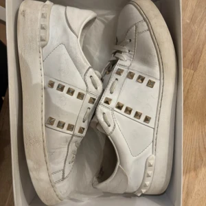 Vita sneakers med nitar från Valentino - Säljer ett par vita sneakers från Valentino i bra skick. De har coola nitar på sidorna och snörning framtill. Perfekta för en stilren look med en edgy twist. Lite smuts på sulorna men annars i fint skick.