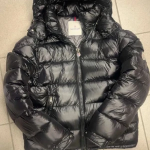 Moncler Maya - Säljer en snygg svart dunjacka från Moncler i mycket bra skick. Jackan har en quiltad design med dragkedja och en cool logga på ärmen. Perfekt för vintern med sin varma och puffiga stil. Den har också en unik serietidningsdetalj på insidan. Passar perfekt för kalla dagar! Oanvänd skick 10/10 endast saker på bilderna till kommer!!!!