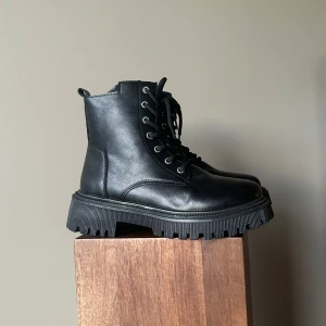 Svarta kängor med foder - Säljer ett par oanvända svarta kängor i skinnimitation med snörning och rejäl sula. De har ett mysigt foder inuti som håller fötterna varma under kalla dagar. Perfekta för höst och vinter! 🖤