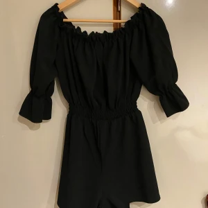 Svart offshoulder jumpsuit från Nelly - Snygg svart offshoulder jumpsuit från Nelly i storlek S. Den har långa puffiga ärmar och en elastisk midja för en bekväm passform. Perfekt för både vardag och festliga tillfällen. 🖤