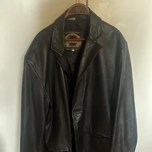 Vintage skinnkavaj  - Säljer en snygg svart skinnjacka från Action i storlek 54. Jackan har en klassisk design med krage och är perfekt för höst och vår. Den är i mycket bra skick och gjord av äkta läder, vilket ger en lyxig känsla. Perfekt för dig som vill ha en tidlös stil!