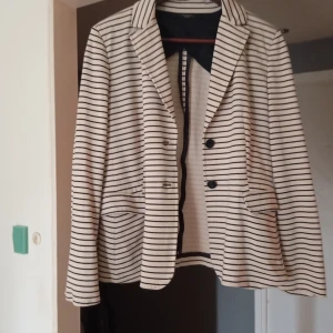 Randig kavaj från MaxMara - Säljer en snygg randig kavaj från MaxMara Weekend. Den är vit med svarta ränder och har en klassisk krage och knappar framtill. Perfekt för både vardag och fest! Passar bra till både jeans och kjol.