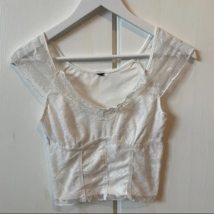 Vit spetsblus - Säljer en superfin vit spetsblus med korta ärmar. Den har ett romantiskt och elegant utseende med vackra spetsdetaljer över hela tyget. Perfekt för sommarens fester eller en stilren vardagslook. Blusen är i mycket bra skick och passar perfekt till både jeans och kjol.