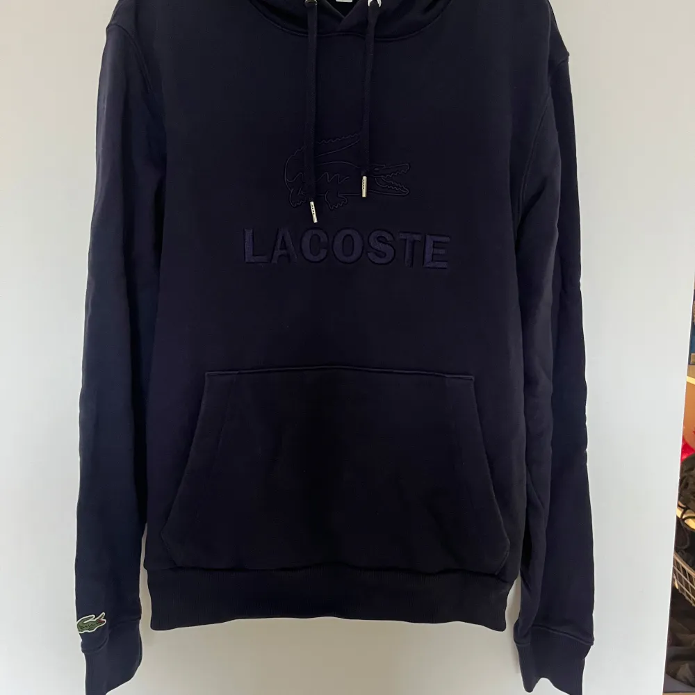 Säljer en snygg mörkblå hoodie från Lacoste i mycket bra skick. Den har en klassisk känguruficka och justerbar huva med dragsko. Perfekt för höst och vinter, och den är supermjuk och bekväm. Passar både till vardags och chillkvällar. 🐊. Tröjor & Koftor.