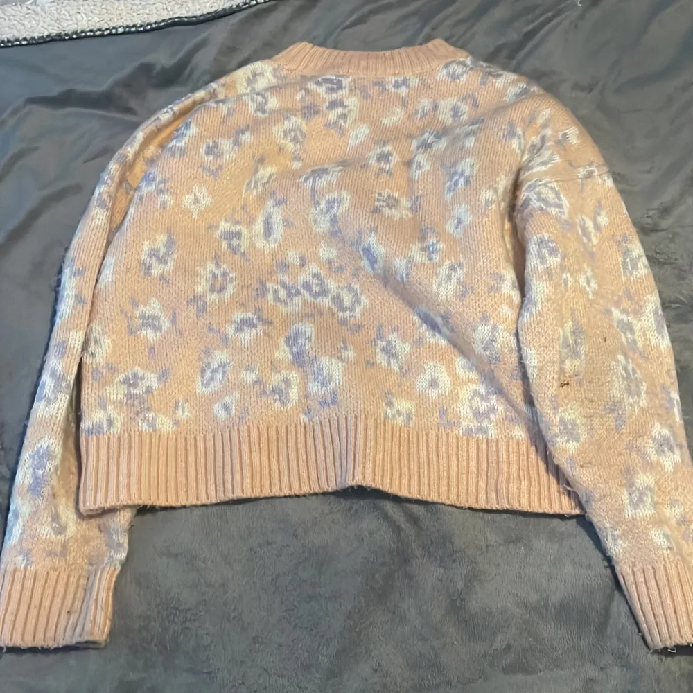 Superfin rosa stickad tröja från Mango med ett subtilt blommönster i vitt och ljuslila. Den har en ribbad kant vid ärmslut och nederkant, vilket ger en snygg finish. Perfekt för kyliga dagar när du vill vara både varm och stilren. . Neuleet.