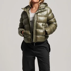Olivgrön pufferjacka från Superdry - Säljer en olivgrön pufferjacka från Superdry i mycket bra skick. Jackan är perfekt för kalla dagar med sin vadderade design och har en praktisk huva. Den har en glansig finish och stängs med dragkedja. Superdry-loggan finns på ärmen. Perfekt för höst och vinter!