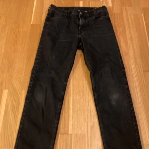Svarta jeansbyxor - Säljer ett par svarta jeansbyxor i bra skick. De har en klassisk design med dragkedja och knappar. Perfekta för både vardag och fest. Passar till det mesta och är ett måste i garderoben! Lite slitna på knäna men inte mer än så. 175 kr ink frakt.