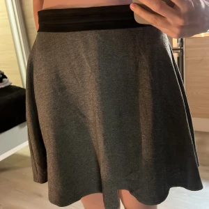 Grå kjol med svart midjeband stl L - Grå kjol med ett svart elastiskt midjeband. Okej skick
