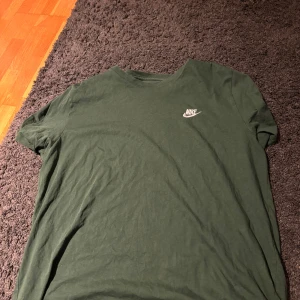 Grön t-shirt från Nike XL - Säljer en snygg grön t-shirt från Nike i bra skick. Den har en klassisk passform och är kortärmad, perfekt för vardagsbruk eller träning. Nike-loggan är tryckt i vitt på bröstet. Skön och enkel stil som funkar året runt! Använd enstaka gånger