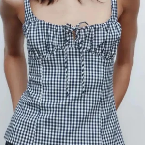 Blårutig linnetopp med knyt - Snygg blårutig linnetopp med smala axelband och knyt framtill. Toppen har en figurnära passform och är perfekt för varma dagar. Mönstret är klassiskt rutigt i blått och vitt.