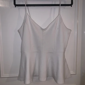 Vit peplum-linnetopp från Gina Tricot - Säljer en vit peplum-linnetopp från Gina Tricot med smala axelband och v-ringning. Toppen har en figurnära passform upptill och en utsvängd nederdel. Perfekt för sommaren och enkel att matcha med jeans eller kjol.