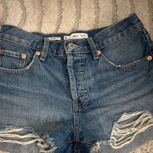 Blå jeansshorts  - Snygga blå jeansshorts från MNG med råa kanter och slitna detaljer framtill. Klassisk femficksmodell med knappar. Perfekta för sommaren 
