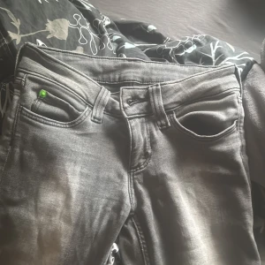 Grå jeans med slitningar - Säljer ett par grå jeans med lätt slitna detaljer och klassisk femficksdesign. Byxorna har en normal passform och är tillverkade i denim. Perfekta för en avslappnad stil.