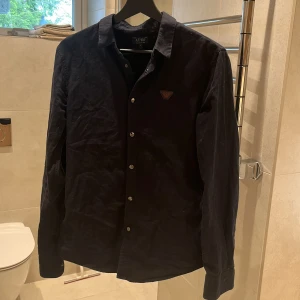 Svart skjorta från Armani Jeans - Säljer en svart skjorta från Armani Jeans med klassisk krage och knappar framtill. Skjortan har ett diskret logomärke på bröstet och är långärmad. Perfekt för dig som gillar stilrena plagg med exklusiv känsla. PRIS LAN DISKUTERAS!