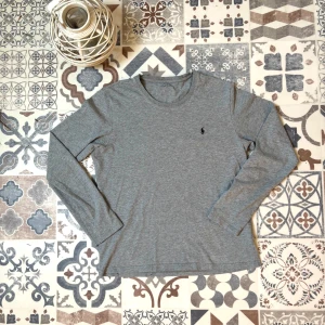 Grå långärmad tröja från Polo Ralph Lauren - Säljer en stilren grå långärmad tröja från Polo Ralph Lauren. Tröjan har rund halsringning och en liten broderad logga på bröstet. Skicket är 10/10, andvänd 2 gånger. Hör av er vid frågor!