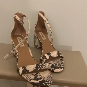 Mönstrade klackskor från Steve Madden - Säljer ett par trendiga klackskor med blockklack från Steve Madden. Skorna har ett mönste i beige, svart och bruna toner samt en smal rem över tårna och runt vristen med spänne. Perfekta för fest eller om man vill ha några fina klackskor!❤️
