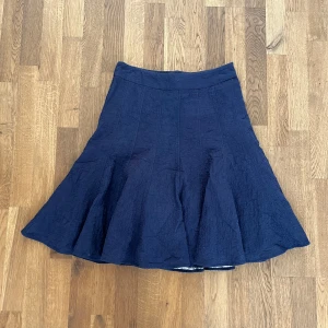 Mörkblå kjol med broderade blommor - Säljer en mörkblå kjol med utsvängd form och fina broderade blommor i tyget. Kjolen har en hög midja och är sydd i ett lätt material som ger ett snyggt fall. Perfekt för dig som gillar diskreta detaljer och stilren design.