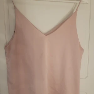 Ljusrosa linnetopp med smala axelband - Säljer en ljusrosa linnetopp med smala axelband och v-ringning. Toppen har en enkel och stilren design, perfekt för varma dagar eller som layering-plagg.