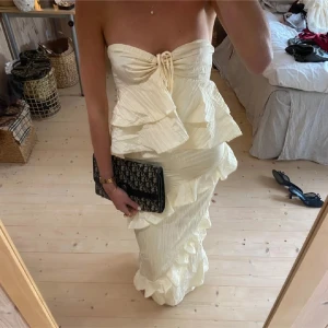 Champagnefärgad långklänning med volanger - Superfin axelbandslös långklänning i champagnefärg med volangdetaljer och knyt framtill. Klänningen har en figurnära passform och är perfekt för festliga tillfällen. (Lånade bilder) den var för liten för mig