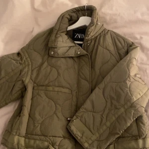 Olivgrön quiltad jacka från Zara - Säljer en olivgrön quiltad jacka från Zara i storlek S. Jackan har hög krage, dragkedja och tryckknappar framtill samt två stora fickor. Den är lätt oversized och har ett snyggt mönster i quiltningen. Perfekt för kyliga dagar.