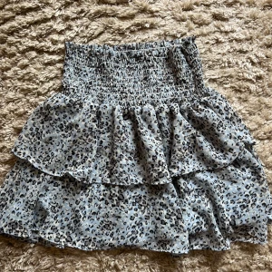 Leopardmönstrad volangkjol från Chelsea - Supersöt kort kjol från Chelsea med leopardmönster och volanger. Kjolen har smock i midjan för en bekväm passform och är perfekt för dig som gillar trendiga detaljer och djurmönster.