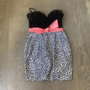 Leopardmönstrad kortklänning med rosett - Säljer en snygg kortklänning med svart överdel, leopardmönstrad kjol och en rosa rosett i midjan. Klänningen har smala axelband och figurnära passform. Perfekt för dig som vill sticka ut! Riktig vintage❤️