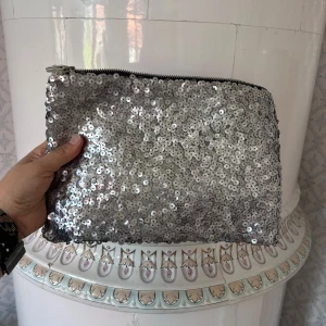Silvrig paljettkuvertväska  - Säljer en glittrig kuvertväska i silver med paljetter över hela ytan. Väskan har dragkedja upptill och är perfekt för att lyfta vilken outfit som helst. Rymmer det viktigaste och är lätt att bära med sig.