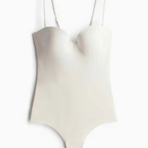 Populär H&M body - Säljer en stilren vit bodysuit med tunna justerbara axelband och formpressade kupor. Materialet är slätt och stretchigt för en bekväm passform. PERFEKT plagg att ha i garderoben nu till sommaren!🍹💓 Storlek 80C. Skulle även kunna passa mindre då axelbanden går att göra tightare! Hör av er vid minsta fundering! Tryck gärna på köp nu!😚 Hade även kunnat tänka mig byta mot en i röd i storlek 75B