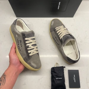 Saint Laurent Skor  - Gråa Saint Laurent-skor – Sällsynt modell  Säljer ett par gråa sneakers från Saint Laurent i en mycket ovanlig modell som inte tillverkas längre. De är svåra att få tag på och passar perfekt för dig som gillar unika skor.  Storlek 40 EU, men Saint Laurent är oftast lite större i storleken – så de kan passa dig som brukar ha 40.5 också.  Detta ingår:  - Originalkartong - Skopåse - Nya reservsnören - Äkthetskort  Skorna är i fint begagnat skick, finns för upphämtning på Lindholmen utanför Göteborg