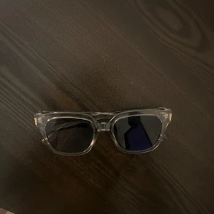 Transparenta solglasögon med svarta glas - Snygga solglasögon med transparent båge och svarta fyrkantiga glas. Bågarna är i plast och har en modern, stilren look som passar till många outfits.