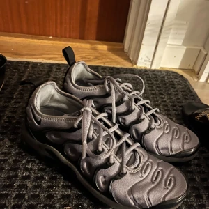 Nike Air Max Plus TN grå sneakers - Säljer ett par grå Nike Air Max Plus TN sneakers med vågig design och synlig Air Max-sula. Skorna har snörning och svart detalj längs sulan. Perfekta för dig som gillar streetwear och sportig stil.
