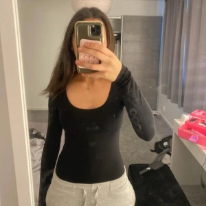 Svart långärmad bodysuit från Gina Tricot - Säljer en svart långärmad bodysuit från Gina Tricot. Den har en rundad urringning och är figurnära i modellen. Perfekt att styla med jeans eller kjol för en enkel och stilren look.