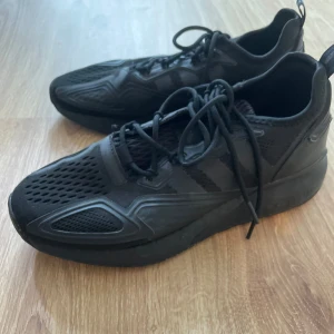 Fotbollsskor för inomhus: Svarta Adidas sneakers storlek 42  - Fotbollsskor för inomhus: Svarta Adidas sneakers med sportig design och diskreta ränder på sidorna. Ovandelen är i mesh och syntet med coola detaljer och snörning. Sulan är robust och ger bra grepp. Perfekta för dig som gillar en clean och modern look.