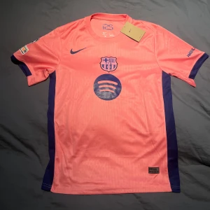  Lamine Yamal rosa matchtröja - Snygg FC Barcelona fotbollströja i rosa med mörkblå detaljer från Nike. Tröjan har korta ärmar, klubbmärke och Spotify-logga på bröstet samt Lamine Yamal och nummer 10 på ryggen. Tillverkad i lätt och ventilerande material, perfekt för match eller träning.                   Tveka inte att höra av er vid minsta fundering 🤙🏻🤙🏻🤙🏻