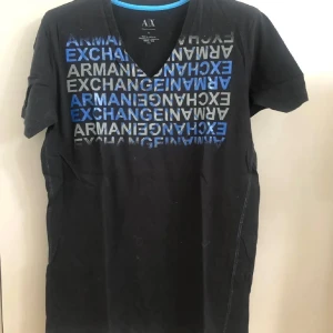 Svart Armani Exchange t-shirt - Svart t-shirt från Armani Exchange med v-ringning och tryck i blått och grått framtill. T-shirten har korta ärmar och är gjord i mjuk bomull. Perfekt för dig som gillar stilrena plagg med en cool logga framtill.