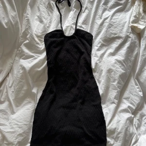 Svart halterneck kortklänning - Snygg svart klänning med halterneck-design och subtilt mönster. Klänningen har en tight passform som framhäver figuren. Oanvänd 