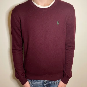Vinröd tröja från Polo Ralph Lauren - Säljer en stilren vinröd tröja från Polo Ralph Lauren. Tröjan har en liten grön logotyp på bröstet och är tillverkad i merinoull.