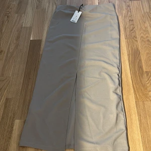 Beige långkjol från 157, XS - Snygg beige långkjol från 157 i stilren design. Kjolen har en rak passform med slits framtill som ger en modern vibe. Perfekt att styla med sneakers eller boots för en clean look.