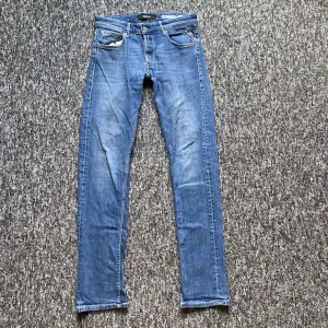 Blå Replay jeans - Säljer ett par klassiska blå jeans från Replay med raka ben och snygga detaljer på bakfickorna. Jeansen har normal passform, fem fickor och är tillverkade i mjukt denimtyg. Perfekta för dig som gillar en tidlös och clean look.
