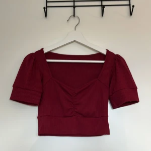 Vinröd croppad ribbad topp - Vinröd croppad topp med ribbad struktur och korta puffärmar. V-ringning framtill med snygg rynkdetalj i mitten. Köpt från okänt märke från Yesstyle.